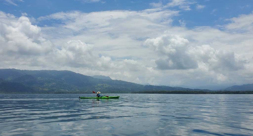 A kayak floats on calm blue water. There is a mountainous landscape in the background. 